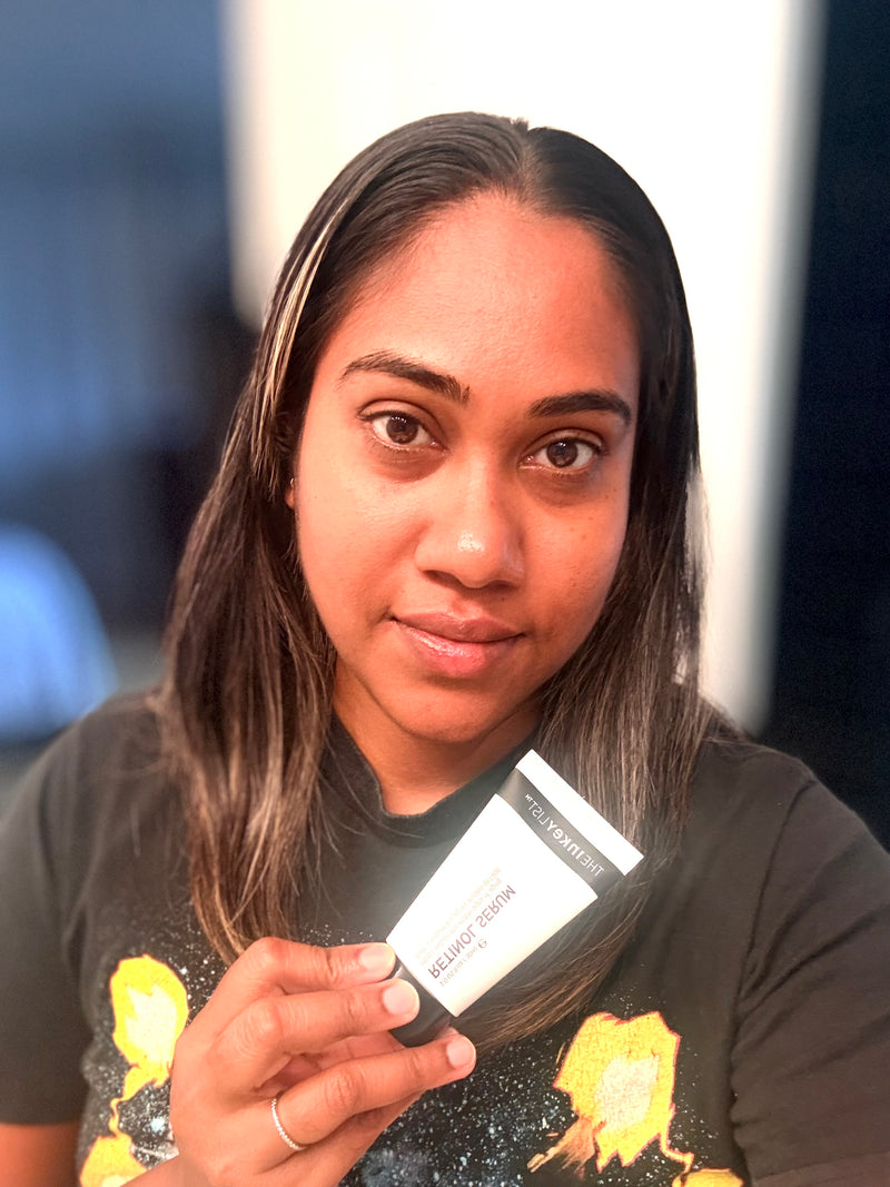A woman holding a small white and black cosmetic pouch labeled 'retinol serum' in front of her face.