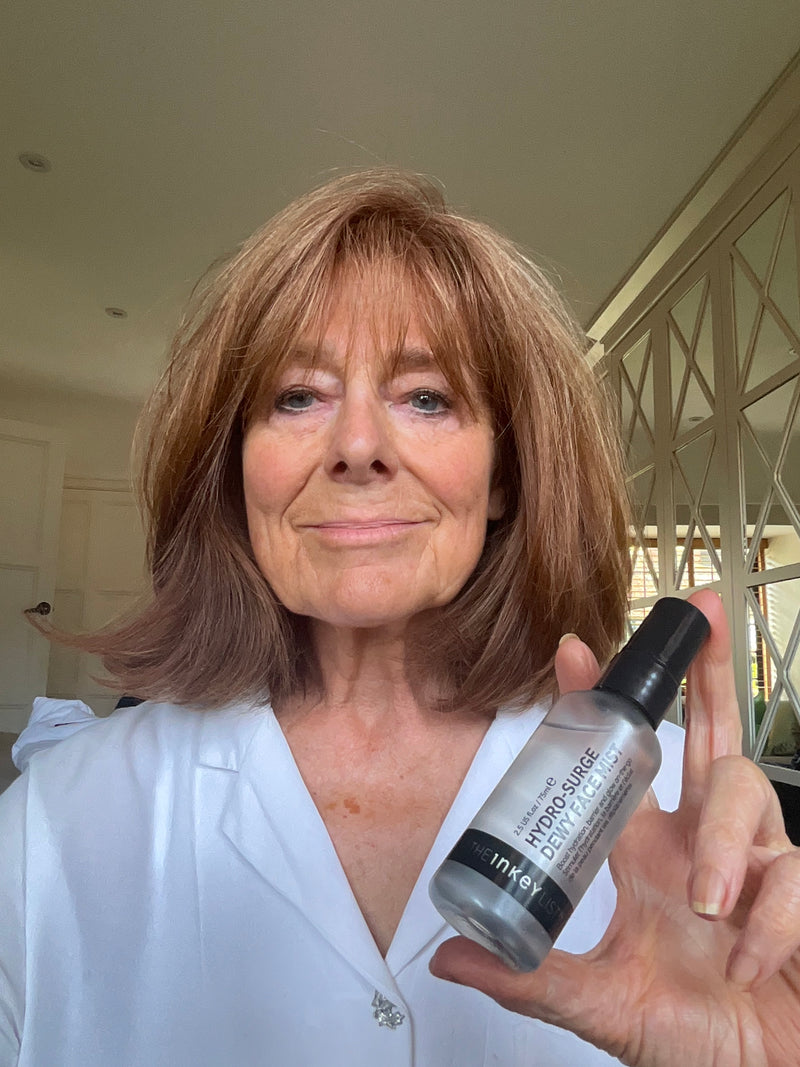A woman with shoulder-length hair holds up a bottle of Mist to show the label.