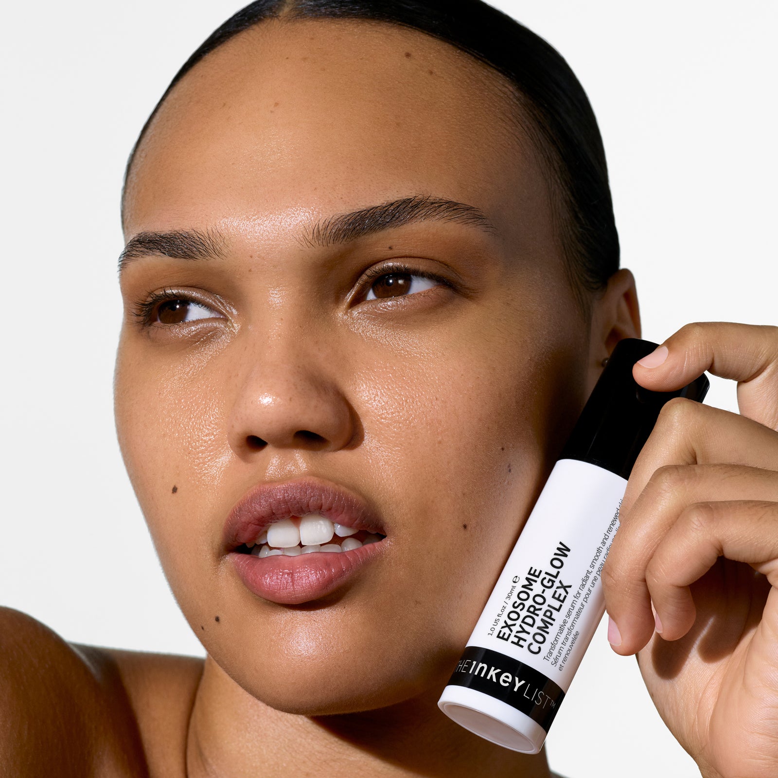 Woman holding a Exosome Hydro-Glow Complex close to her face against a white background