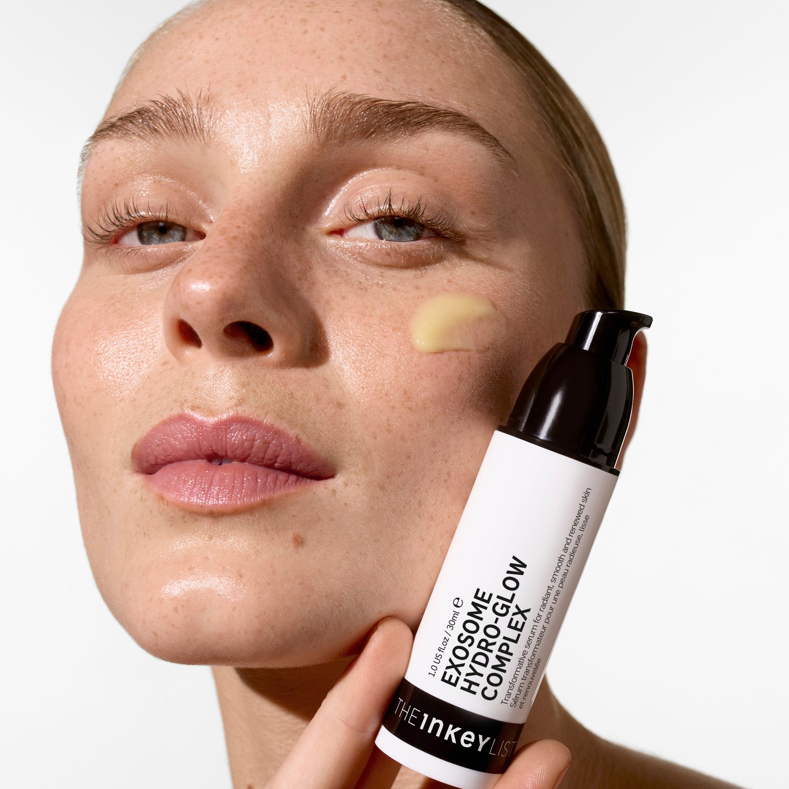 Woman applying Exosome Hydro-Glow Complex to her face with a white background