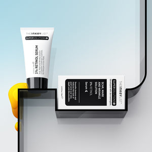 Scar, Mark & Wrinkle Solution tube and outer packaging on a black shelf against blue gradient background with yellow goop