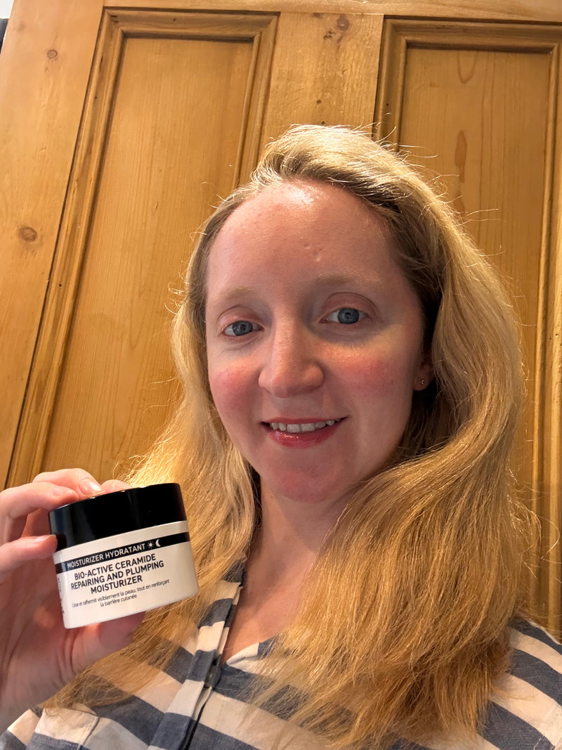 A woman with blonde hair holds a jar of Bio active moisturiser in front of a wooden door background.