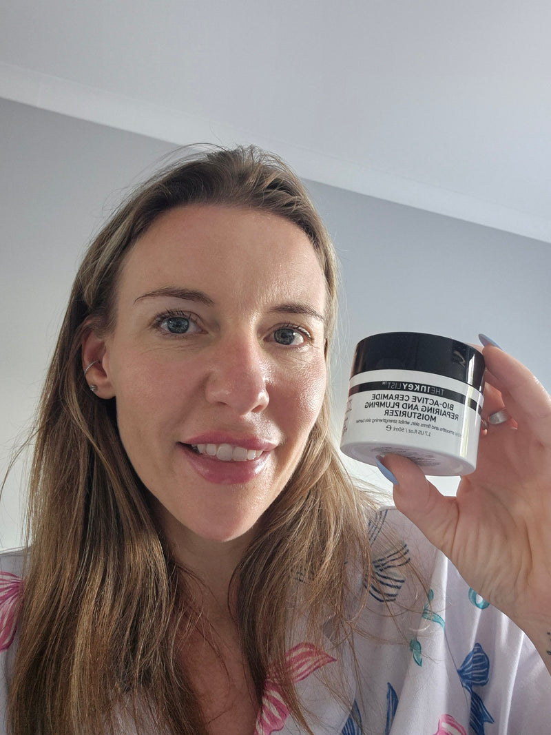 A woman holding up a jar of Bio Active Moisturiser against a plain indoor wall background.