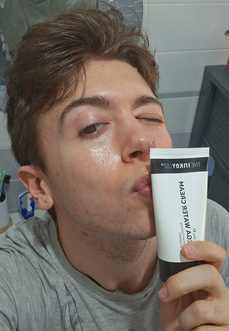 A man in a gray t-shirt holding a white and black tube to his lips in a bathroom setting.