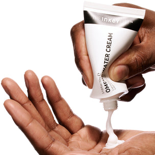 Hand holding a tube of The Inkey List Omega Water Cream with cream being squeezed out.