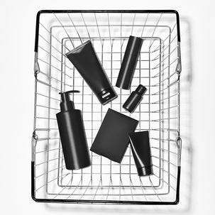 Black skincare products in a wire basket on a white background