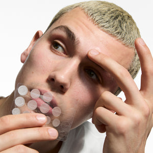 Person applying a transparent sheet to their face with a neutral background