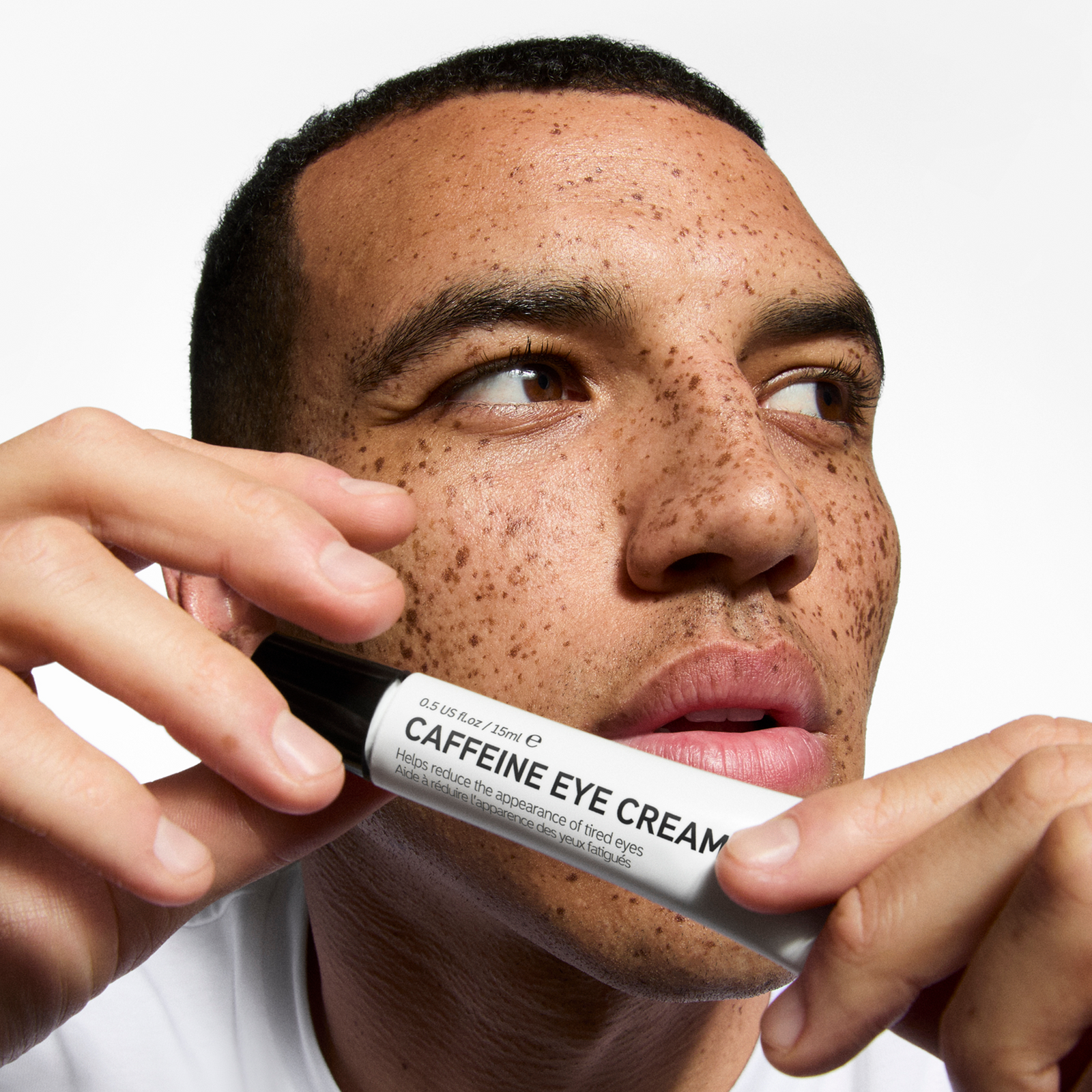Man holding a bottle of caffeine eye cream close to his face