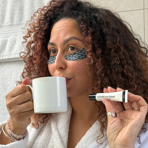 Woman holding a mug and a tube of caffeine eye cream with text on her face.