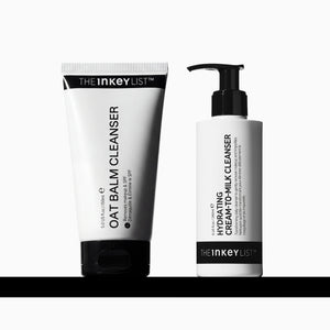 Two skincare products from The Inkey List on a white background with a black horizontal bar at the bottom. On the left is a white squeeze tube labeled 'OAT BALM CLEANSER' with a black cap.