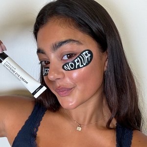 Woman holding a tube of eye cream with 'NO FLUFF' label on her face.