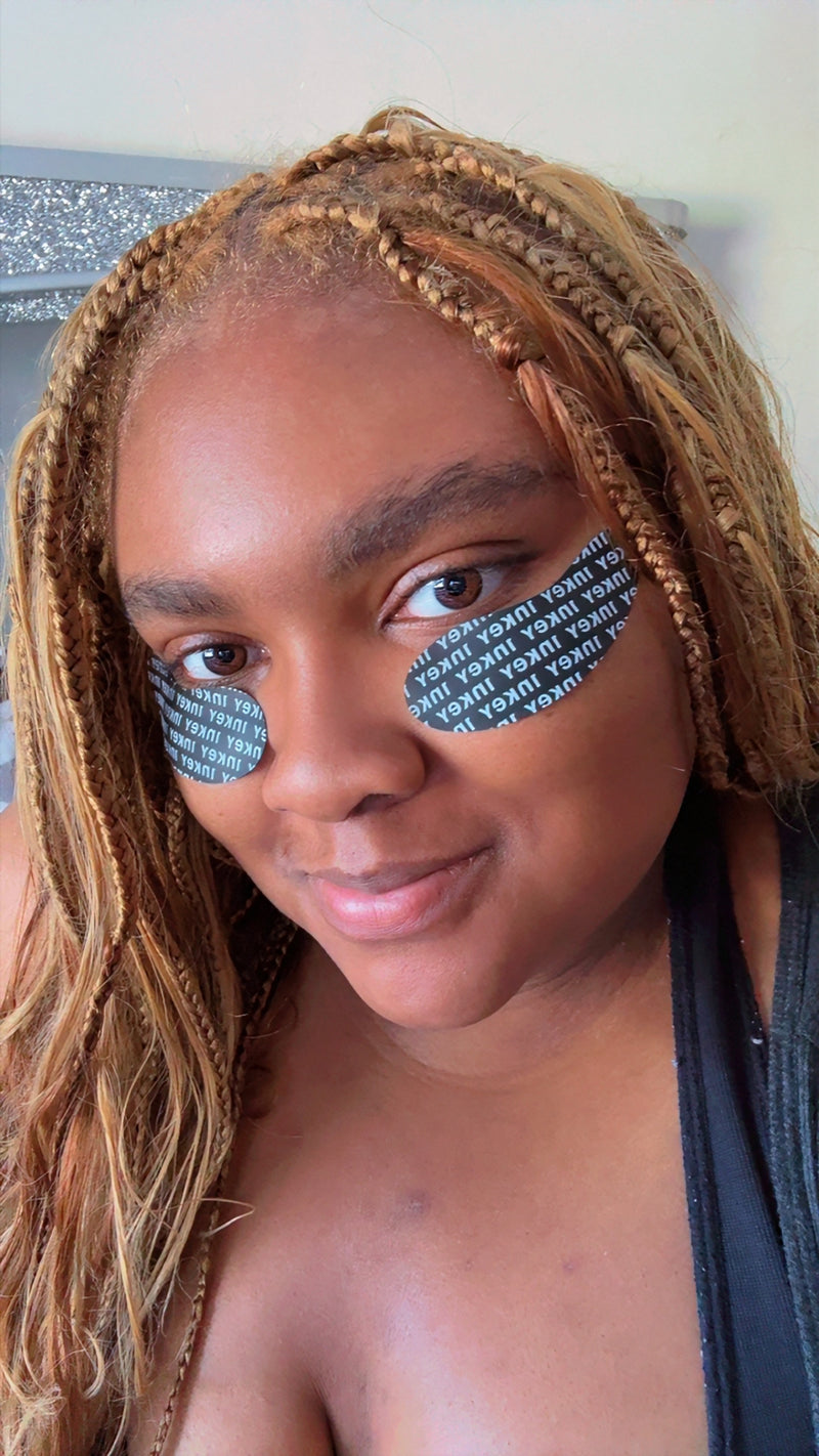 A close-up selfie of a woman with braided hair wearing black and white patterned eye patches under her eyes.