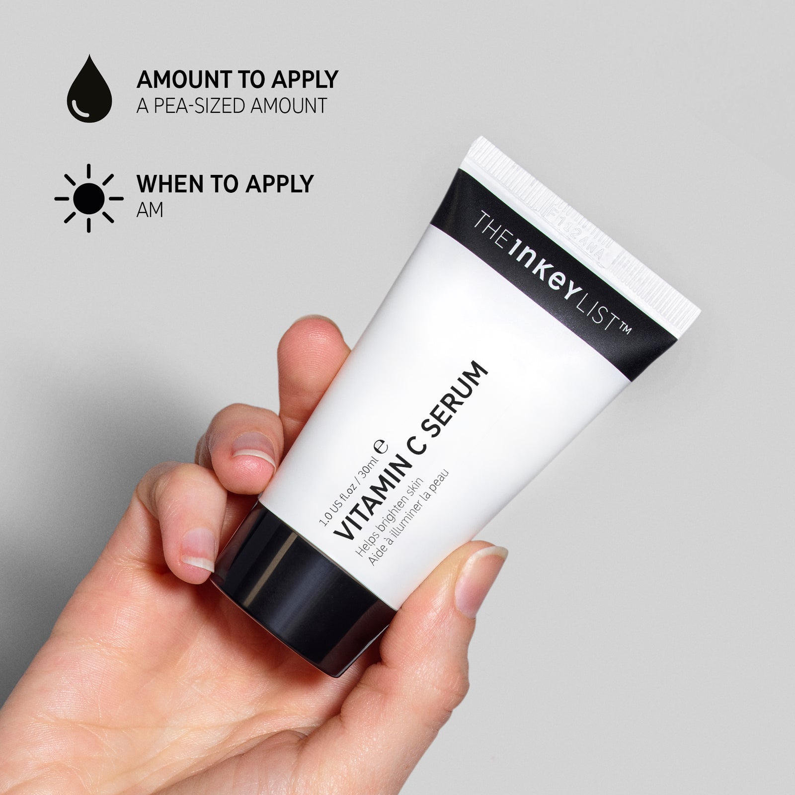 Hand holding a tube of Vitamin C Serum against a grey background annotated with black text to explain amount to apply (pea-sized amount) and when to use it in your skincare routine (AM only)